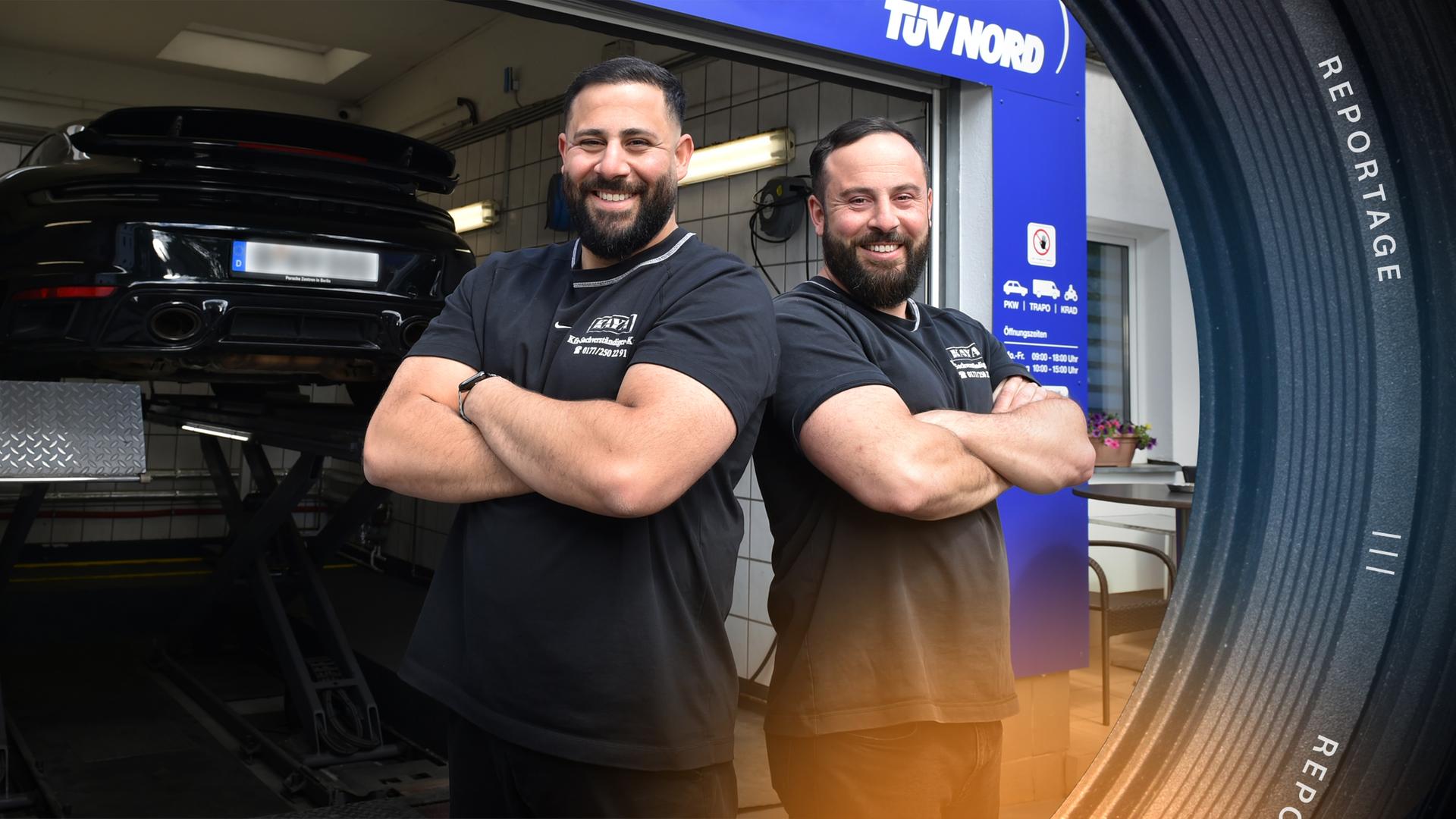 Serkan und Engin Kaya stehen lachend, mit verschränkten Armen und Schulter an Schulter vor einem geöffneten Werkstatttor. Im Hintergrund steht ein Auto auf einer Hebebühne.