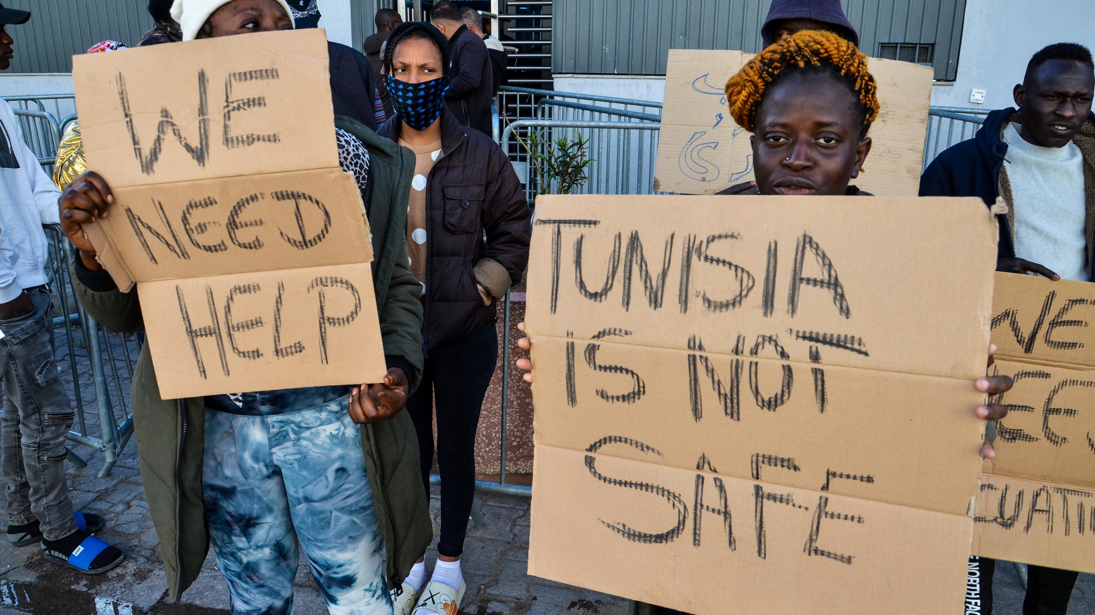 Migranten in Tunesien halten Schilder hoch, auf denen u. a. steht: Tunesien ist nicht sicher