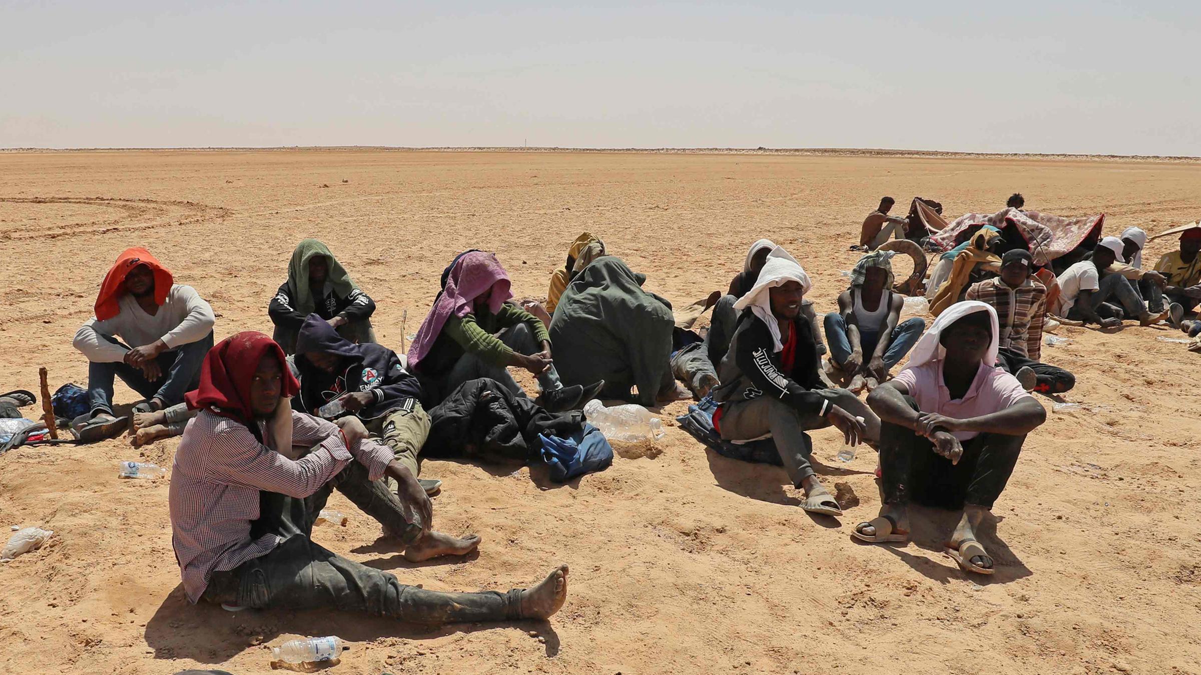 Migranten aus Ländern südlich der Sahara sitzen am 16.07.2023 in der Nähe der libyschen Grenzstadt Al-Assah.