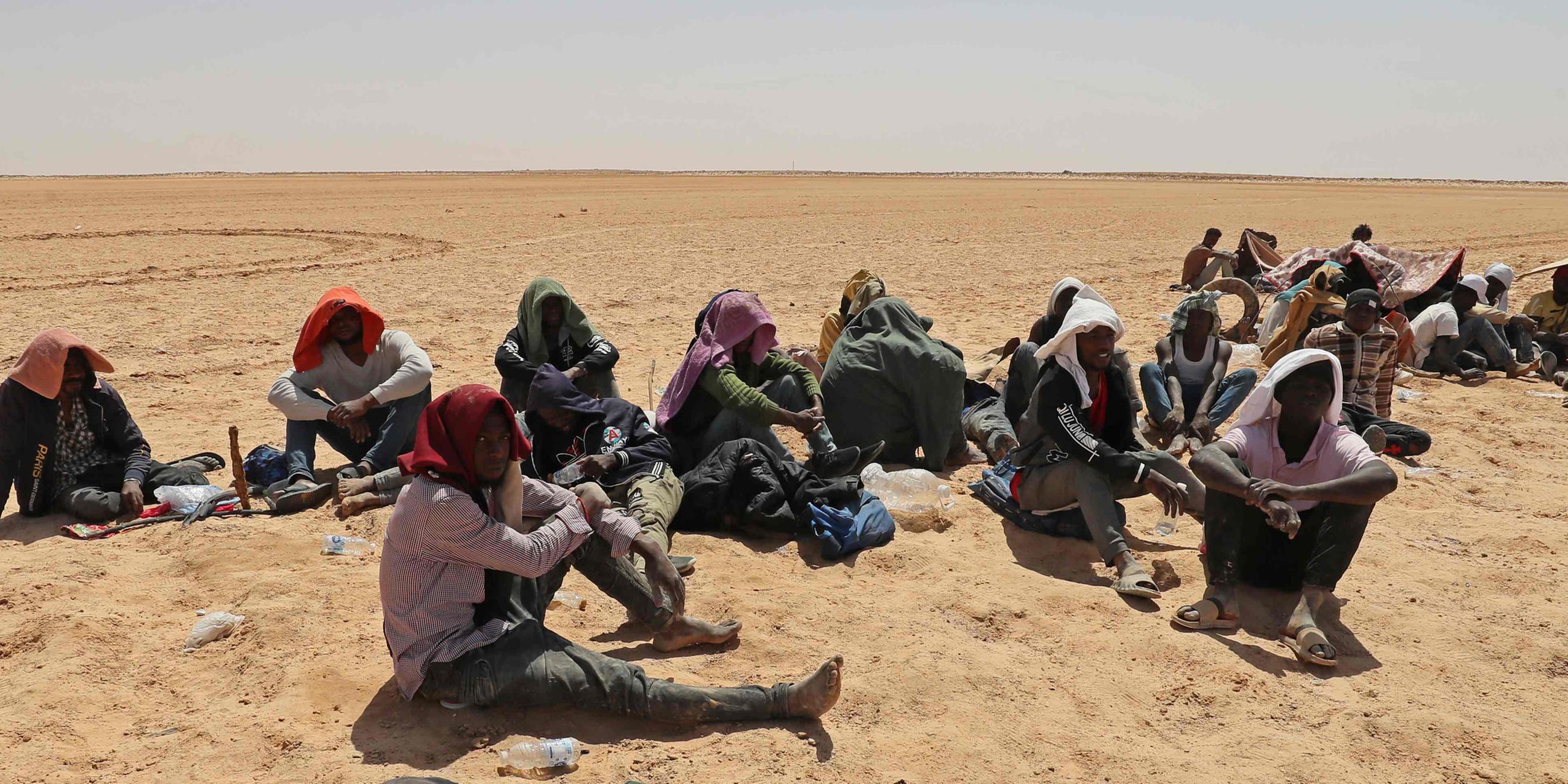 Migranten aus Ländern südlich der Sahara sitzen am 16.07.2023 in der Nähe der libyschen Grenzstadt Al-Assah.