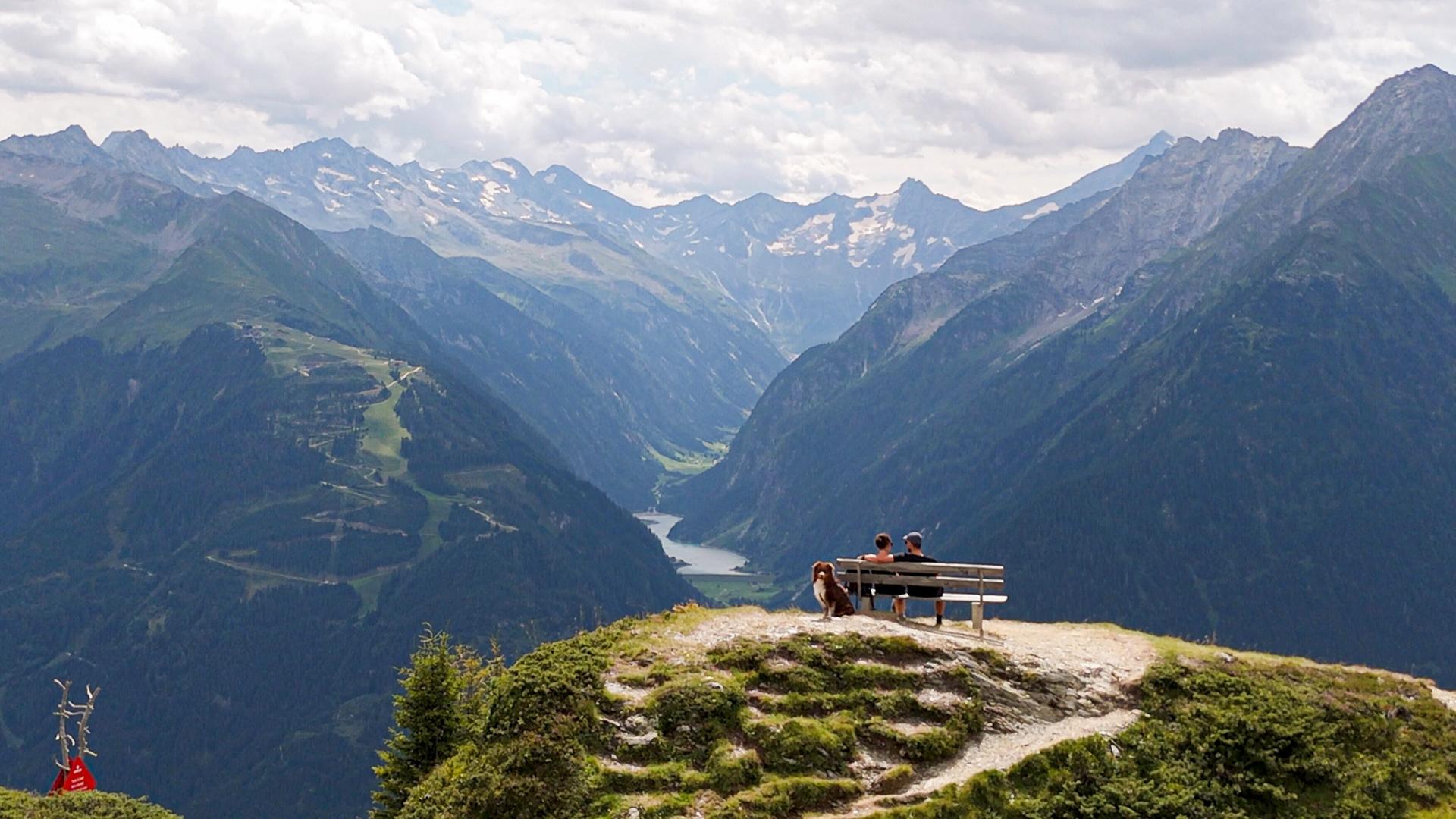 Paar auf einer Bank, sie blicken von oben auf einen See