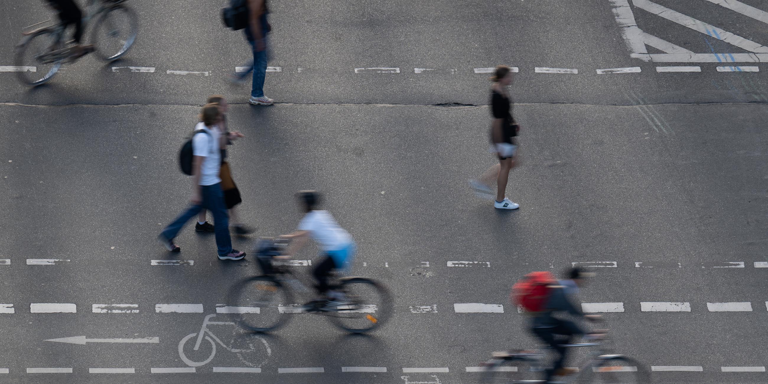 Fußgänger und Radfahrer bewegen sich auf einem Fußgänger- und Fahrradübergang auf einer Straße.