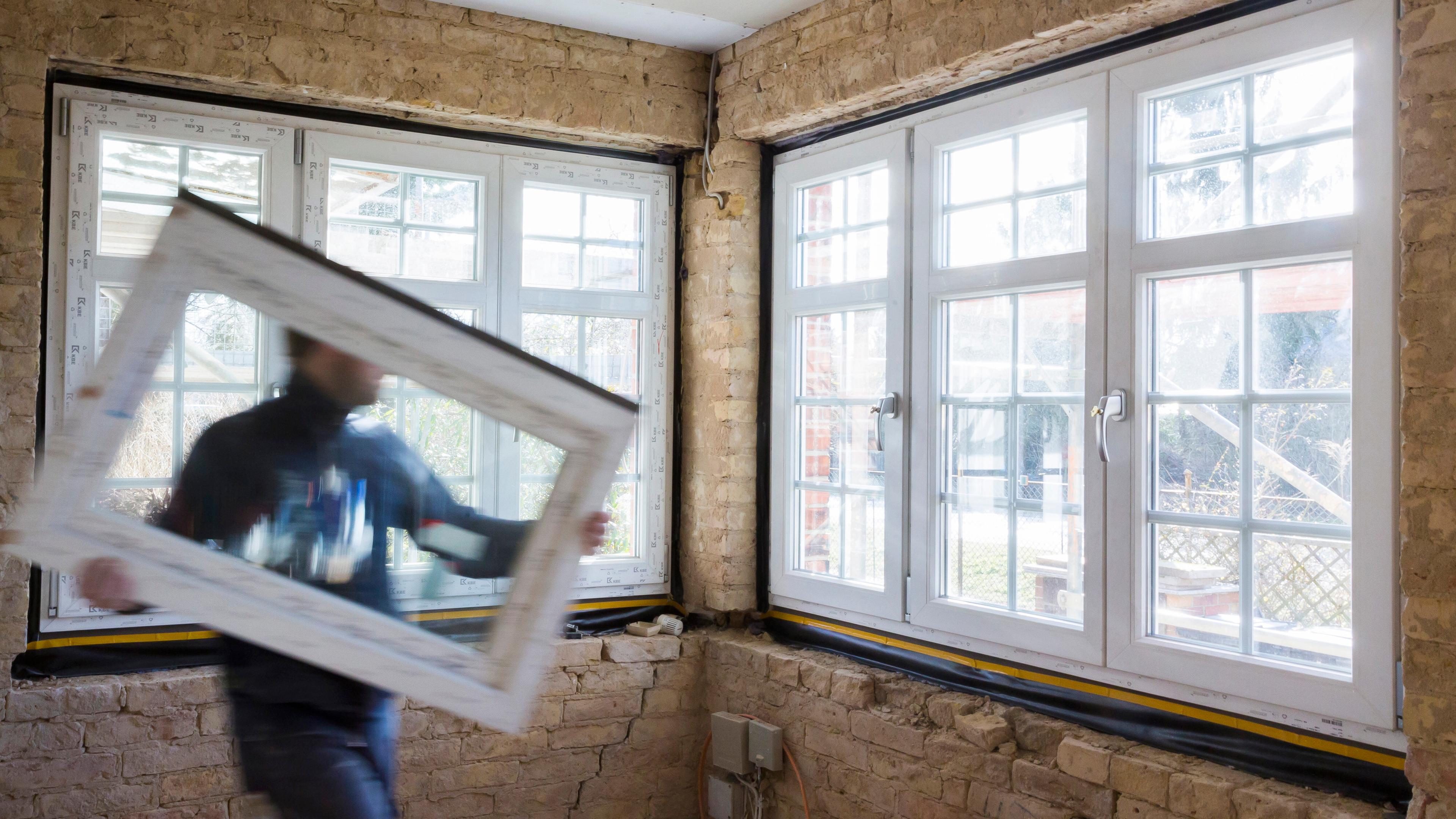 Ein Mann trägt ein neues Fenster in einem Haus, das saniert wird.