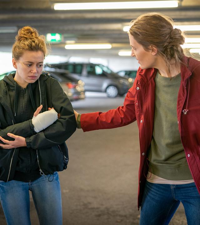 "Notruf Hafenkante - Überlebenskampf": Pola (Alexandra Pfeifer) und ihre Mutter Lena (Nora Moltzen) stehen in einem Parkhaus nebeneinander. Lena zieht ihre Tochter am Arm. Sie hat sich zu ihr gedreht. Pola blickt nachdenklich ins Leere. Sie hält sich ihren rechten eingegipsten Arm.