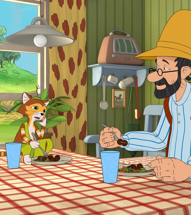 Pettersson sitzt am Esstisch, auf dem Findus im Schneidersitz Platz genommen hat. Beide haben einen gefüllten Teller und ein Glas vor sich stehen.