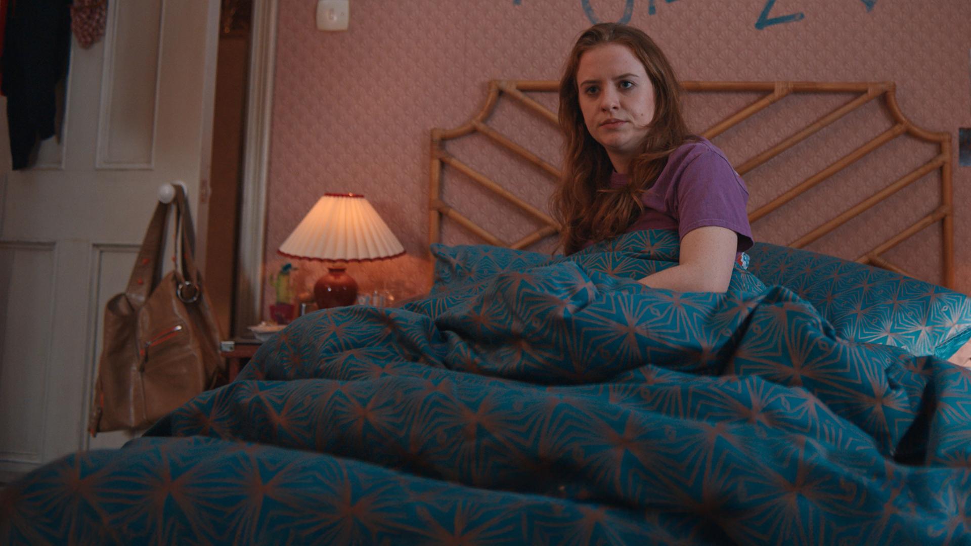 "Extraordinary - Überraschung": Jen (Máiréad Tyers) liegt in ihrem Bett und mustert ihr Schlafzimmer mit skeptischem Blick. Auf der Tapete hinter ihr steht in blauer Farbe an die Wand geschrieben "jen loves jizz".