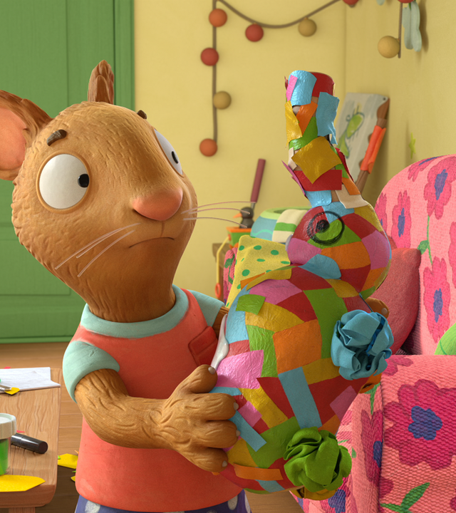 Posy hält ein Geschenk in der Hand, das mit vielen Papierstücken verpackt ist. Es hat die Form eines Elefanten.