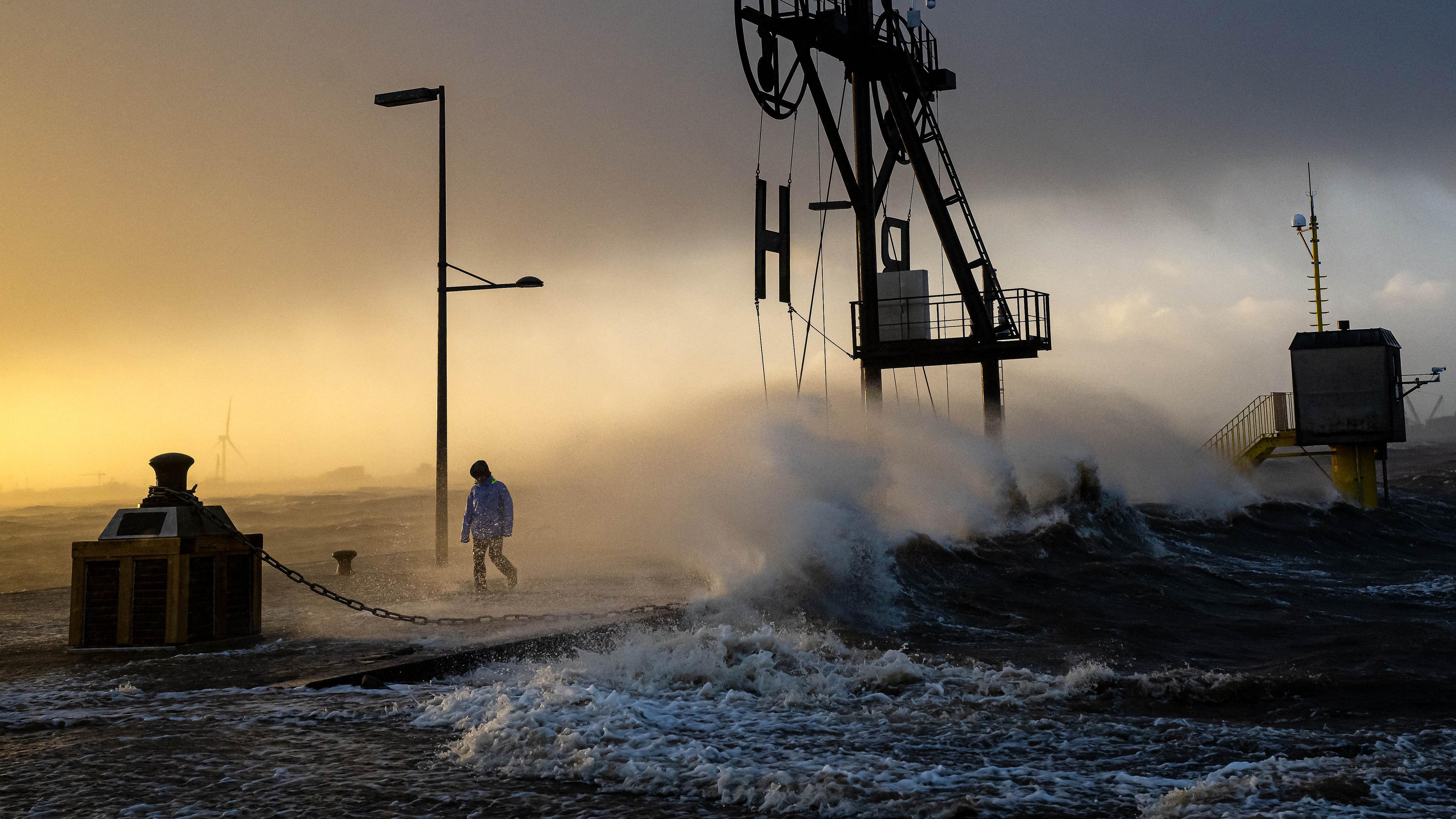 Ein Spaziergänger läuft bei Sturmflut und Wellen am Ufer der Wesermündung in Bremerhaven entlang, aufgenommen am 22.12.2023