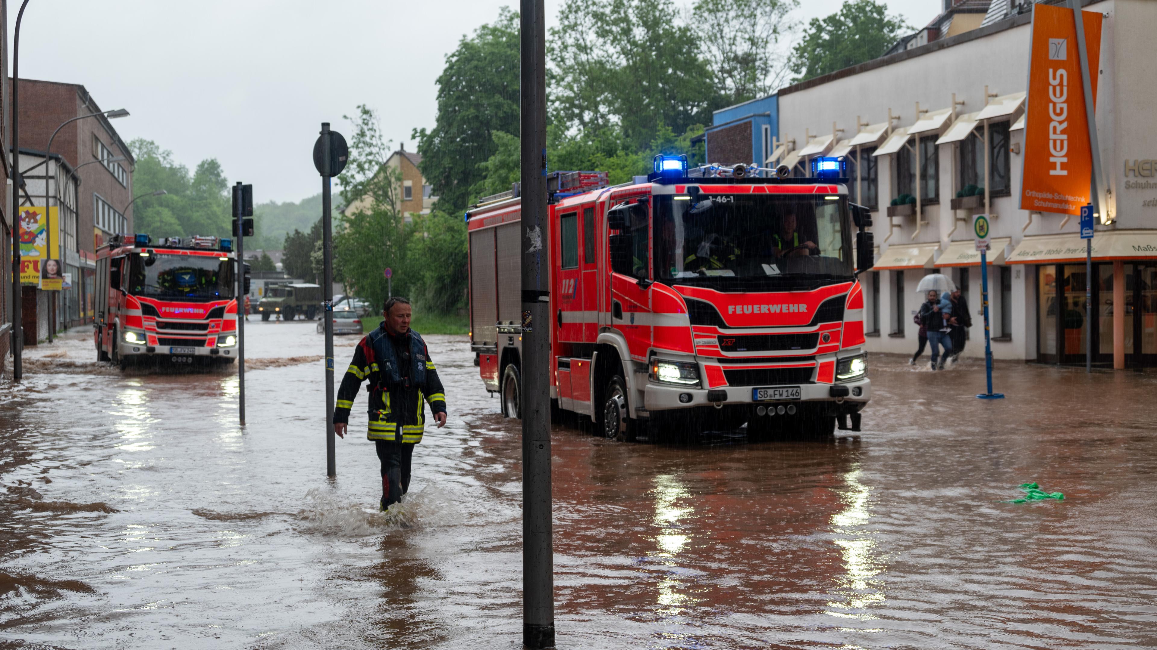 Saarland, Saarbrücken: Feuerwehrleute bewegen sich und ihre LKW durch das Hochwasser in der Fischbachstrasse in Saarbrücken. Nach starken Regenfällen steht diese teilweise unter Wasser.