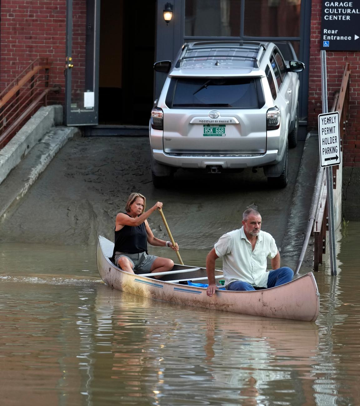 Ein Mann und eine Frau sitzen in einem Kanu und paddeln damit durch ein überschwemmtes Gebiet in Montpelier.