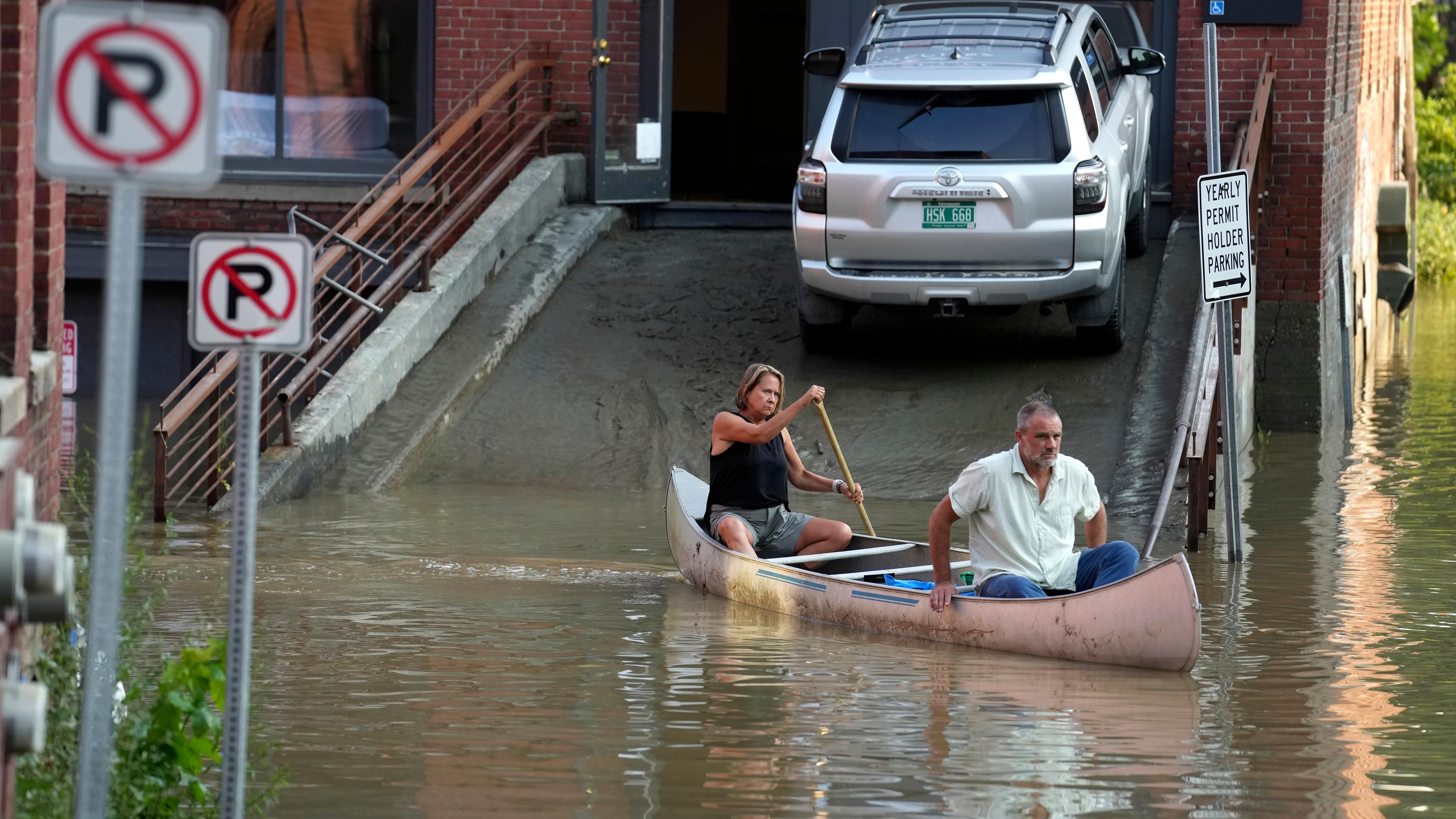 Ein Mann und eine Frau sitzen in einem Kanu und paddeln damit durch ein überschwemmtes Gebiet in Montpelier.