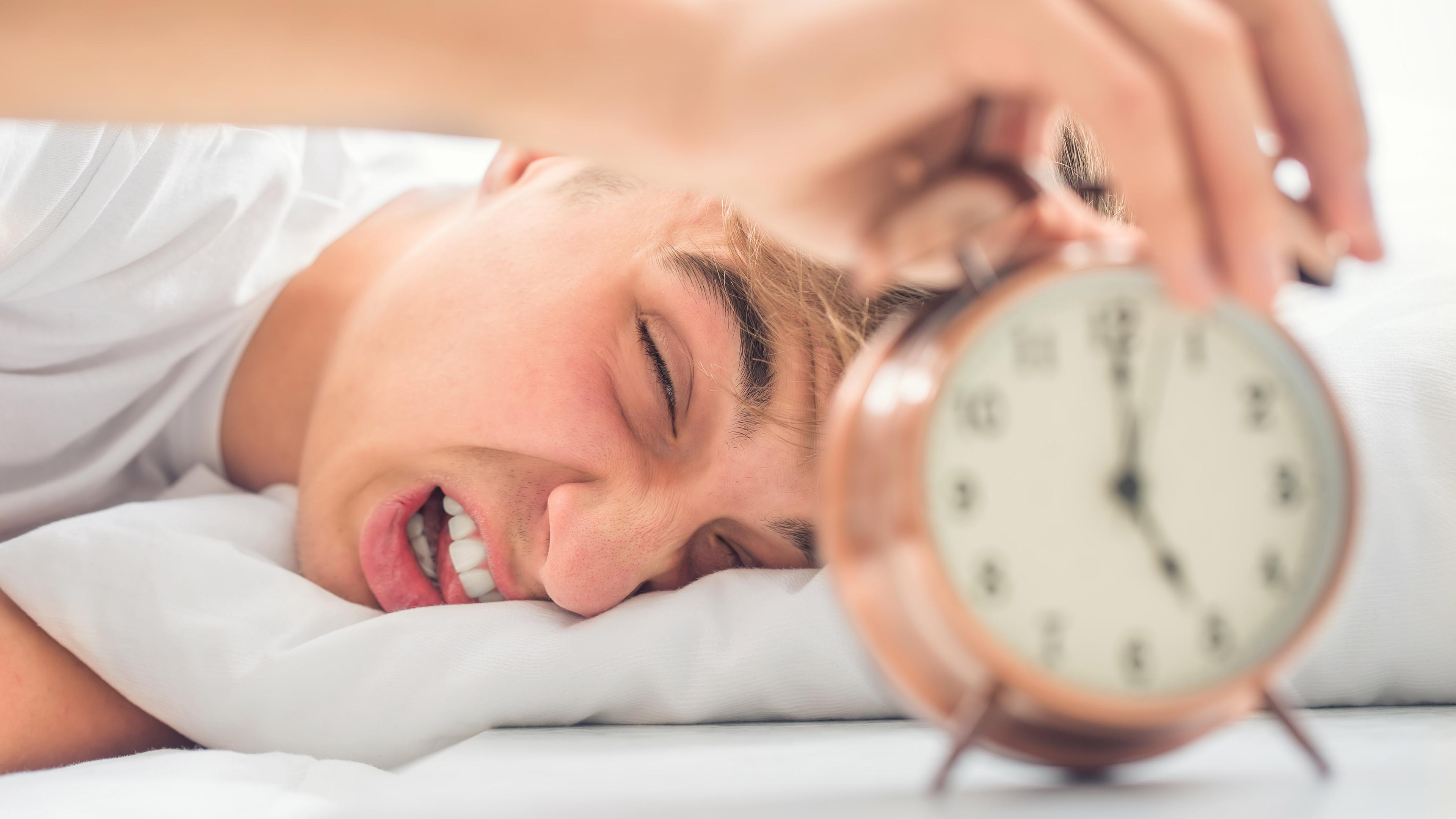 Junger Mann macht ärgerlich den Wecker aus