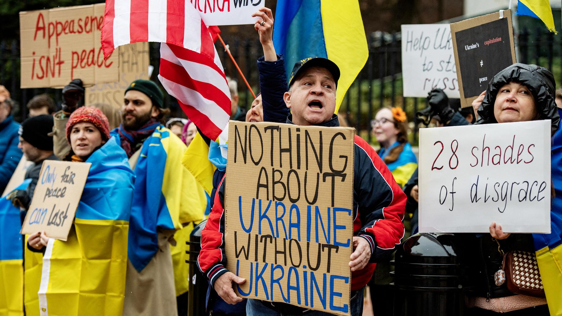 Demonstranten mit gelb-blauen ukrainischen Flaggen halten Plakate hoch, auf denen sie einen Mitbestimmung der Ukraine bei Friedensverhandlungen fordern.