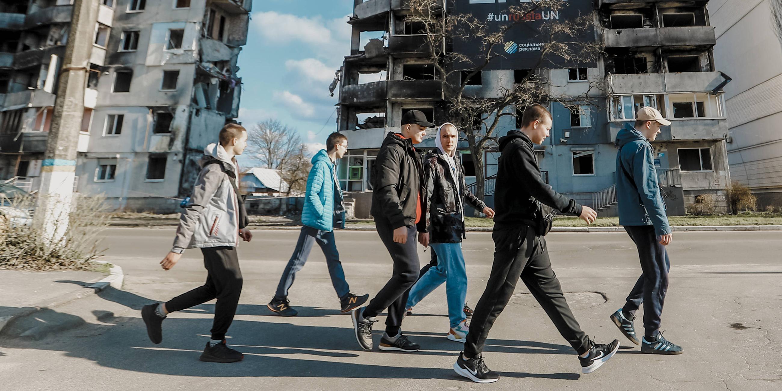 Junge Menschen gehen in Borodyanka in Kiew in der Nähe von zerstörten Wohngebäuden vorbei.