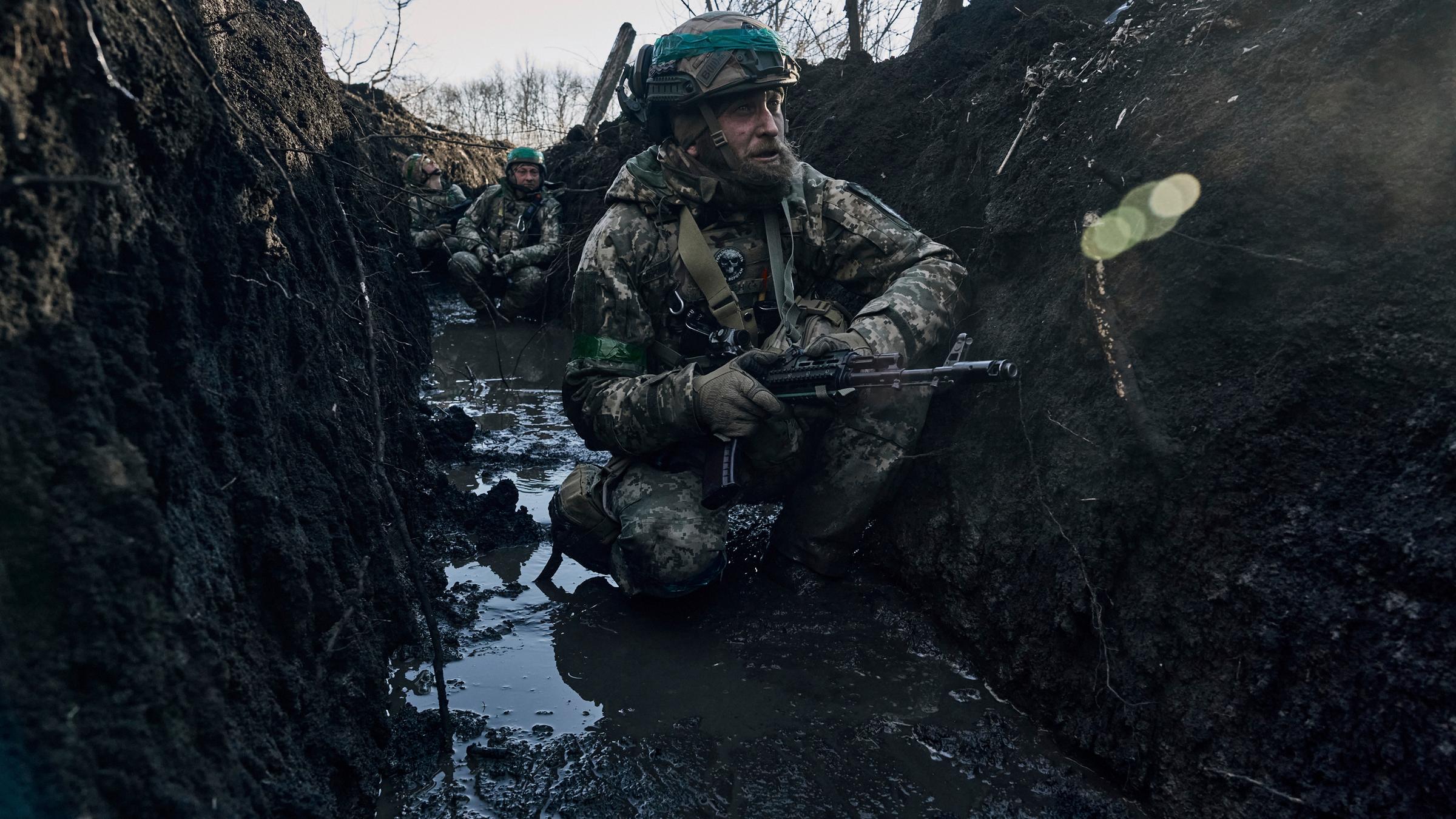 Ukraine, Bachmut: Ukrainische Soldaten hocken im Schlamm in einem Schützengraben unter russischem Beschuss an der Frontlinie in der Nähe von Bachmut.