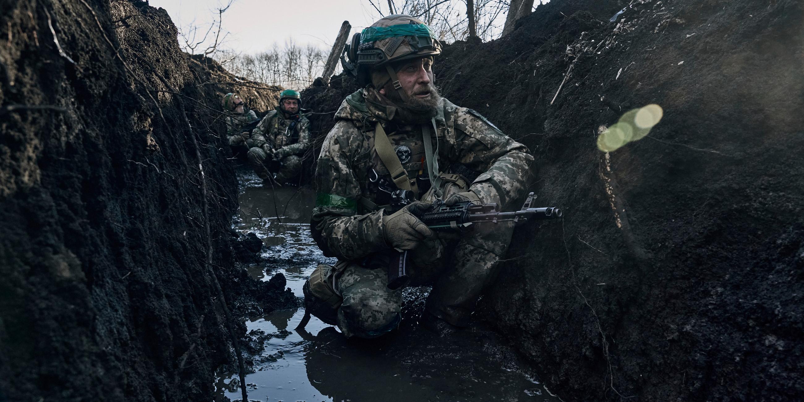 Ukraine, Bachmut: Ukrainische Soldaten hocken im Schlamm in einem Schützengraben unter russischem Beschuss an der Frontlinie in der Nähe von Bachmut.