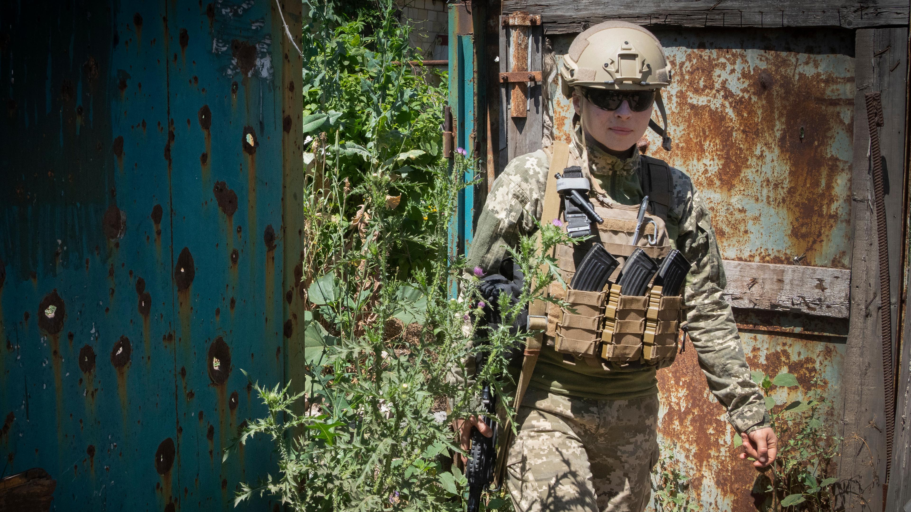 A Ukrainian soldier is advancing at a position in the Donetsk region.  A metal wall with bullet holes on the left.