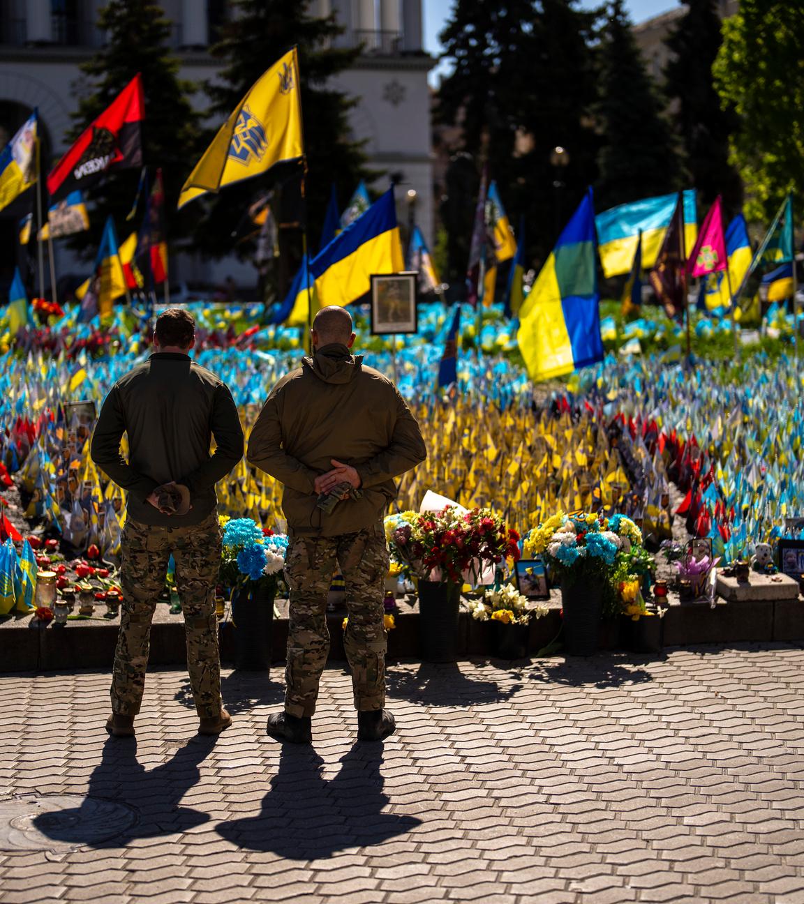 Ukrainian service men stand next to Ukrainian flags and photographs placed in memory of civilians and soldiers killed during the war, at the Independence square in central Kyiv, Saturday, April 20, 2024. 