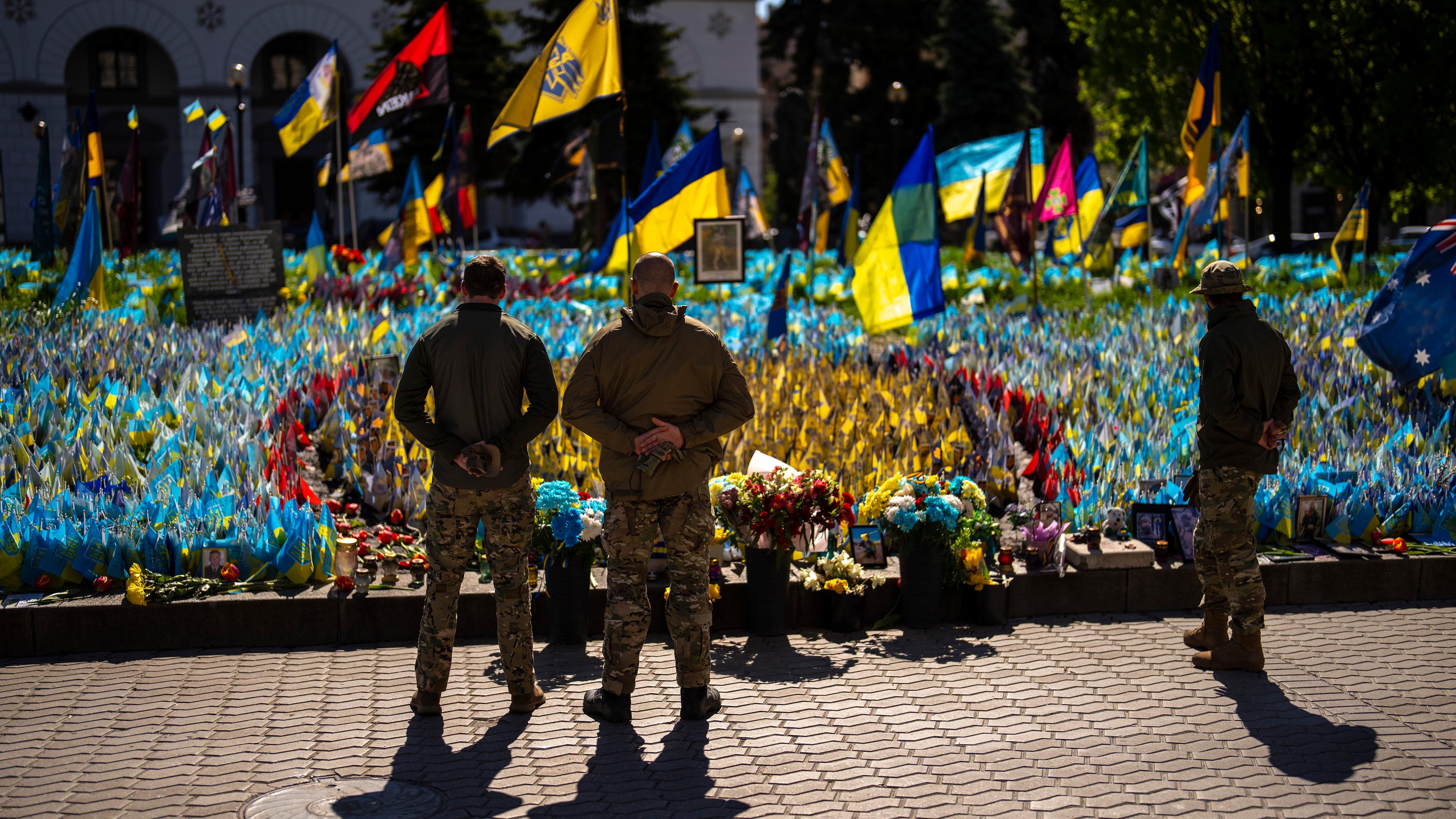 Ukrainian service men stand next to Ukrainian flags and photographs placed in memory of civilians and soldiers killed during the war, at the Independence square in central Kyiv, Saturday, April 20, 2024. 
