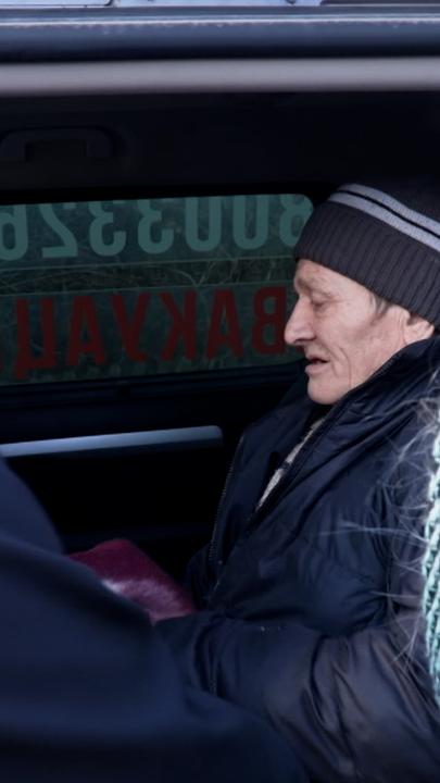 Ein älterer Mann sitzt in einem Auto und trägt eine Mütze