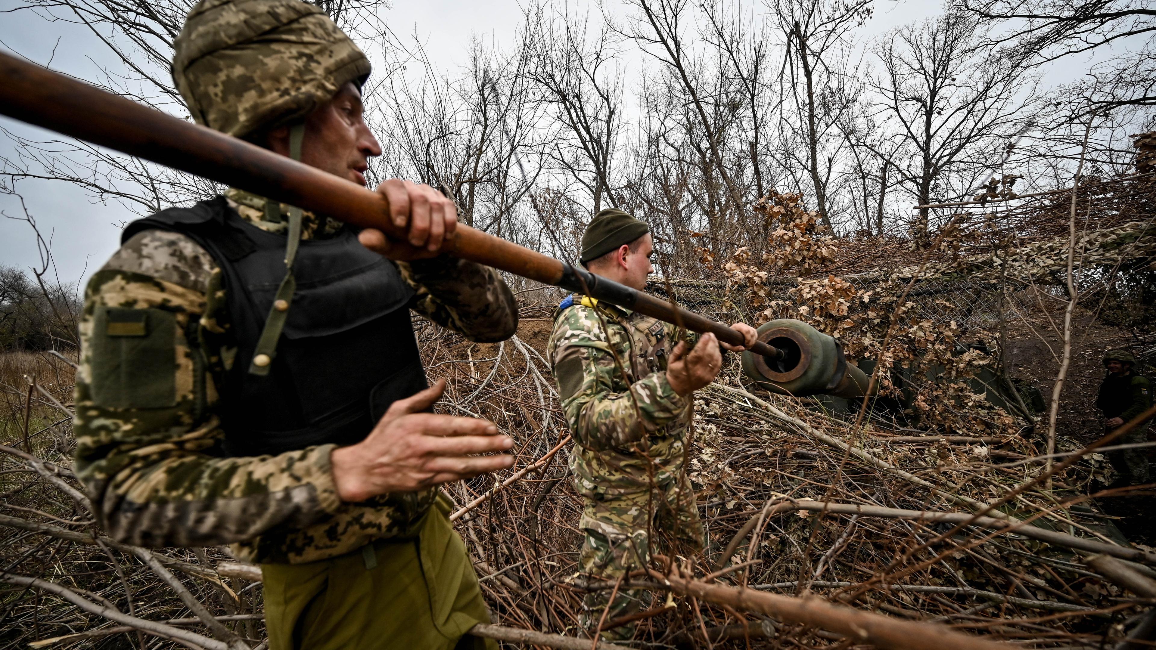 Ukraine, Saporischschja: Zwei Soldaten der Panzerartillerie der 65. mechanisierten Brigade der ukrainischen Streitkräfte reinigen das Rohr einer getarnten selbstfahrenden Panzerhaubitze.
