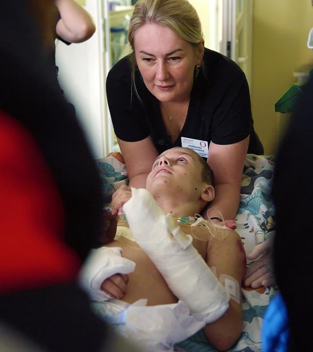 Ein Junge mit verbundenem Rumpf und Armen wird von Helfern auf eine Trage gebettet.