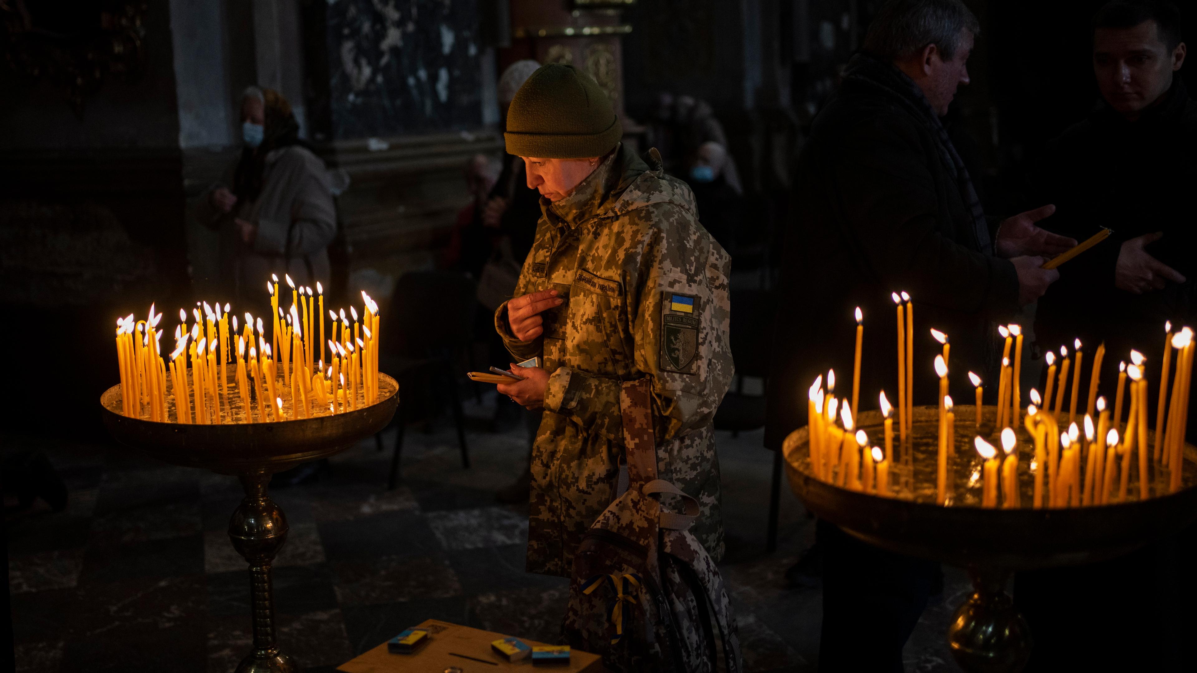 Eine Ukrainerin, gekleidet in eine Militär-Ausrüstung, steht in einer Kirche in der westukrainischen Stadt Lwiw, in der Kerzen brennen.