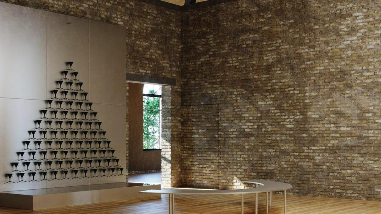 Zu sehen ist ein heller Raum mit Steinwänden, in dessen Mitte eine halbmond-runde Bank steht, von der aus man auf eine dreiecksförmige Skulptur aus Trichtern blicken kann.