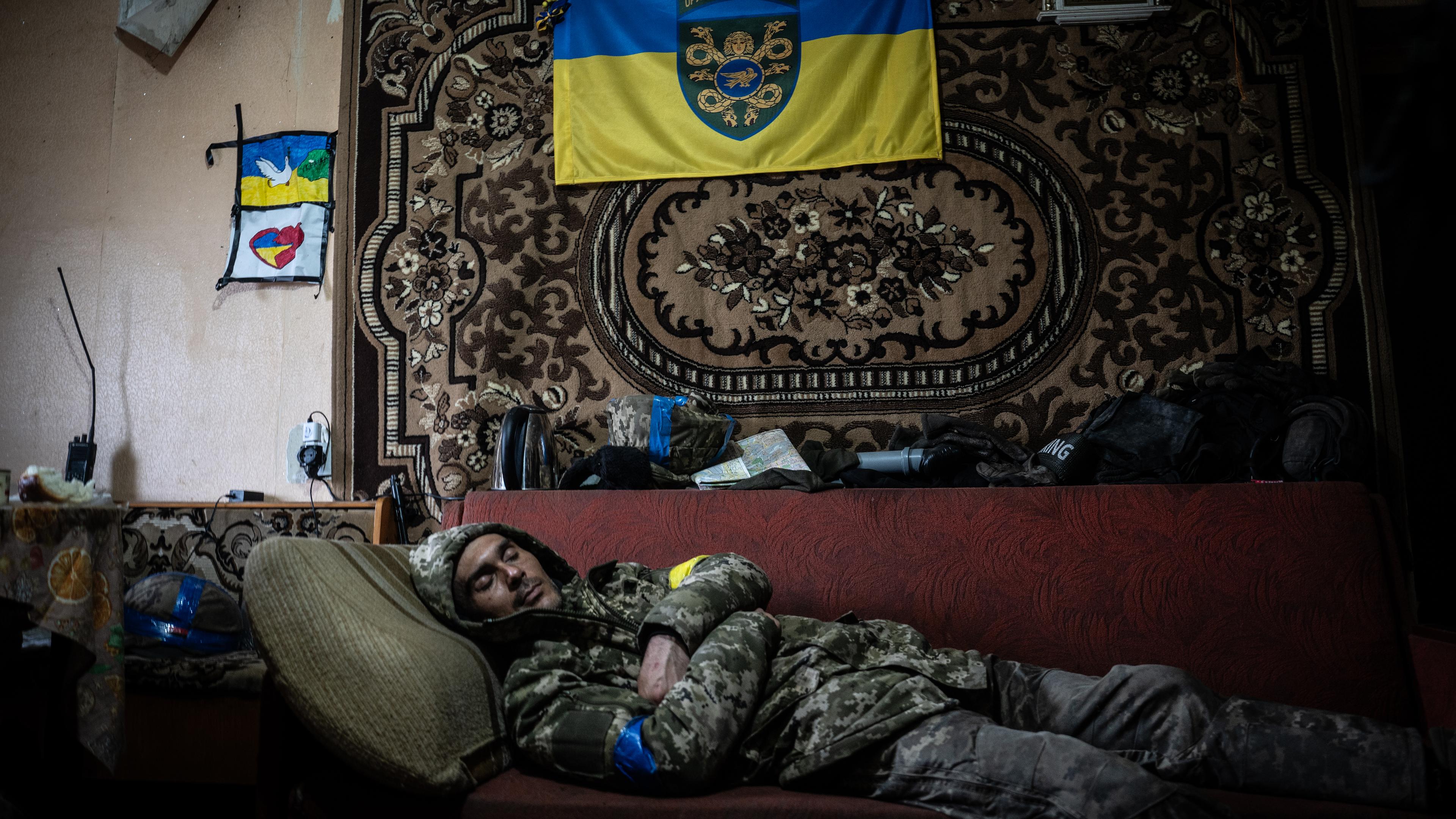 Ein Mann schläft auf einer Couch, über ihm hängt die ukrainische Flagge.