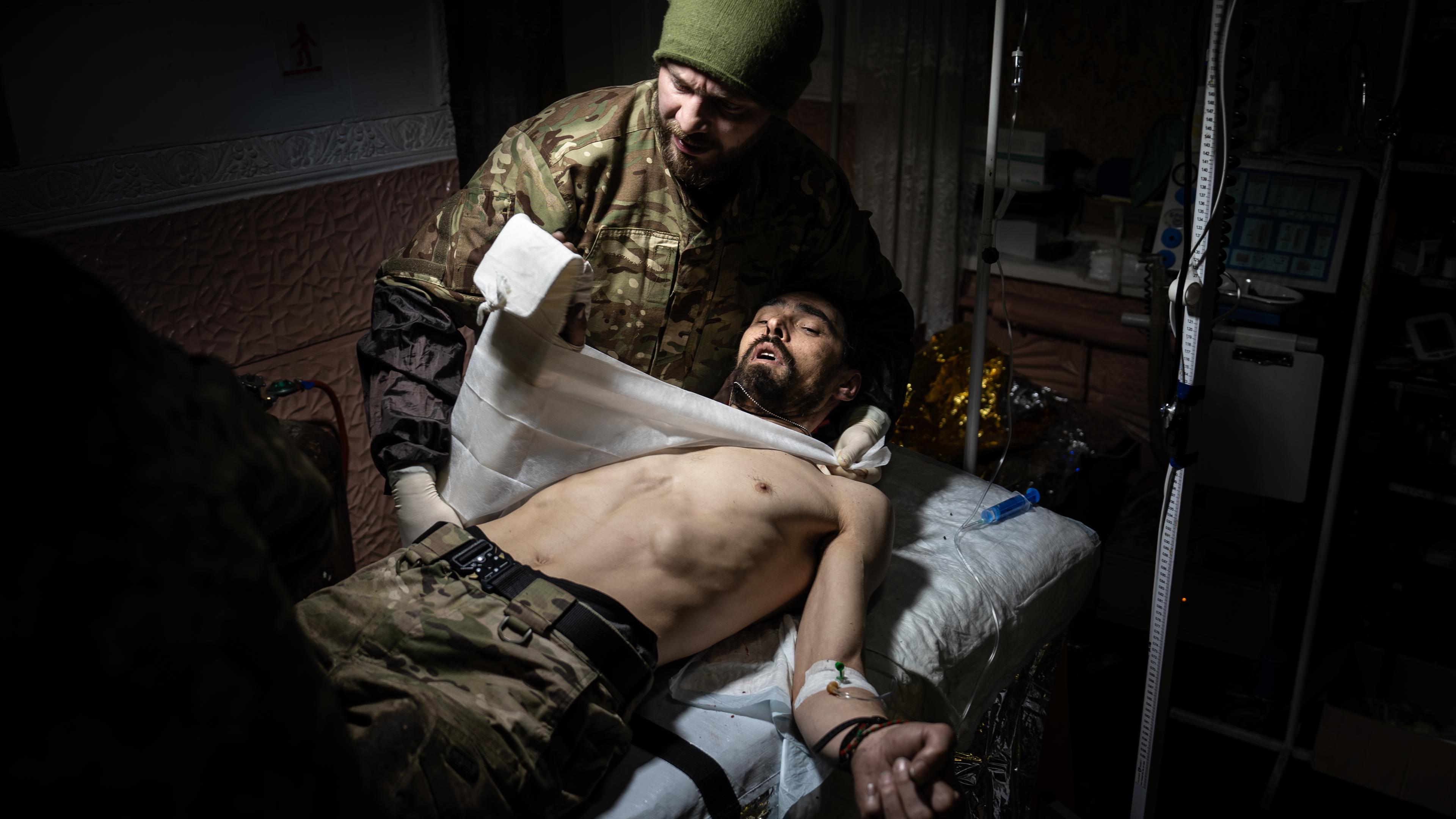 Ein verwundeter Soldat liegt auf einem Bett und wird behandelt.