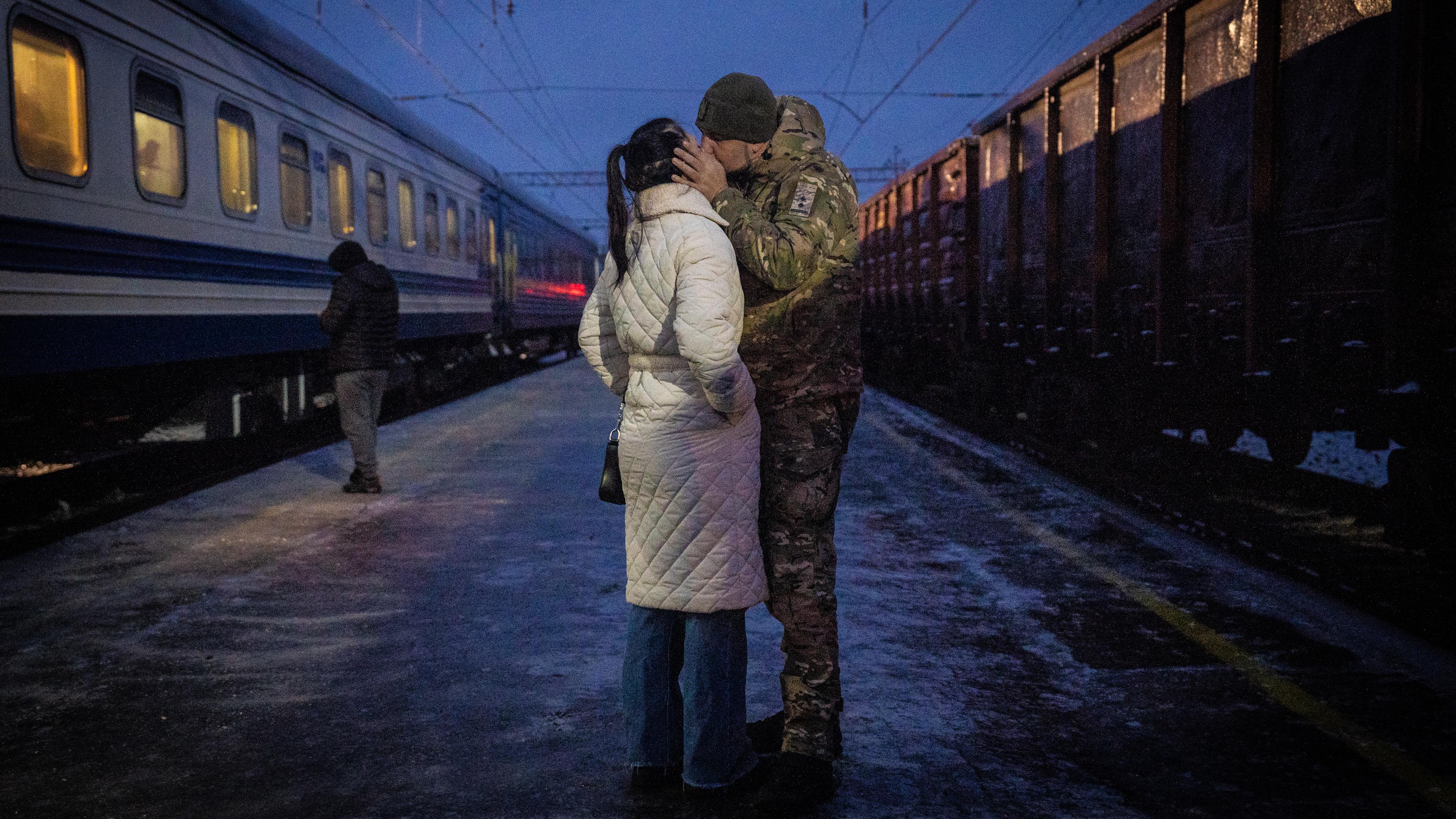Eine Frau und Mann küssen sich auf einem Bahnsteig.