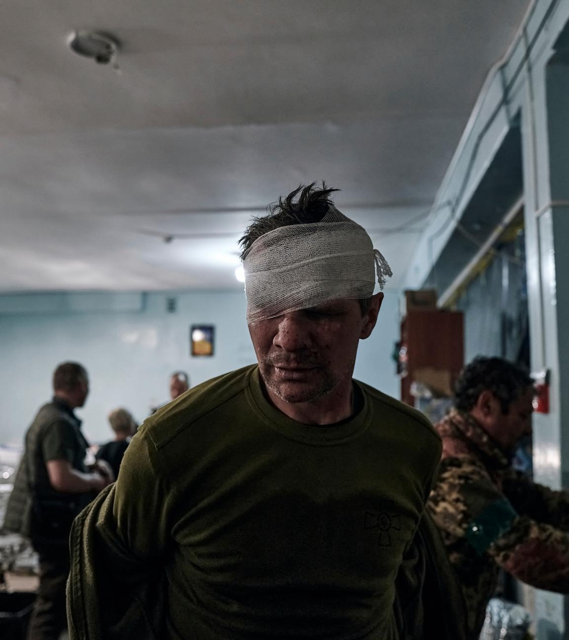 Ein ukrainischer Soldat trägt einen Verband am Kopf, im Hintergrund sind weitere Soldaten.