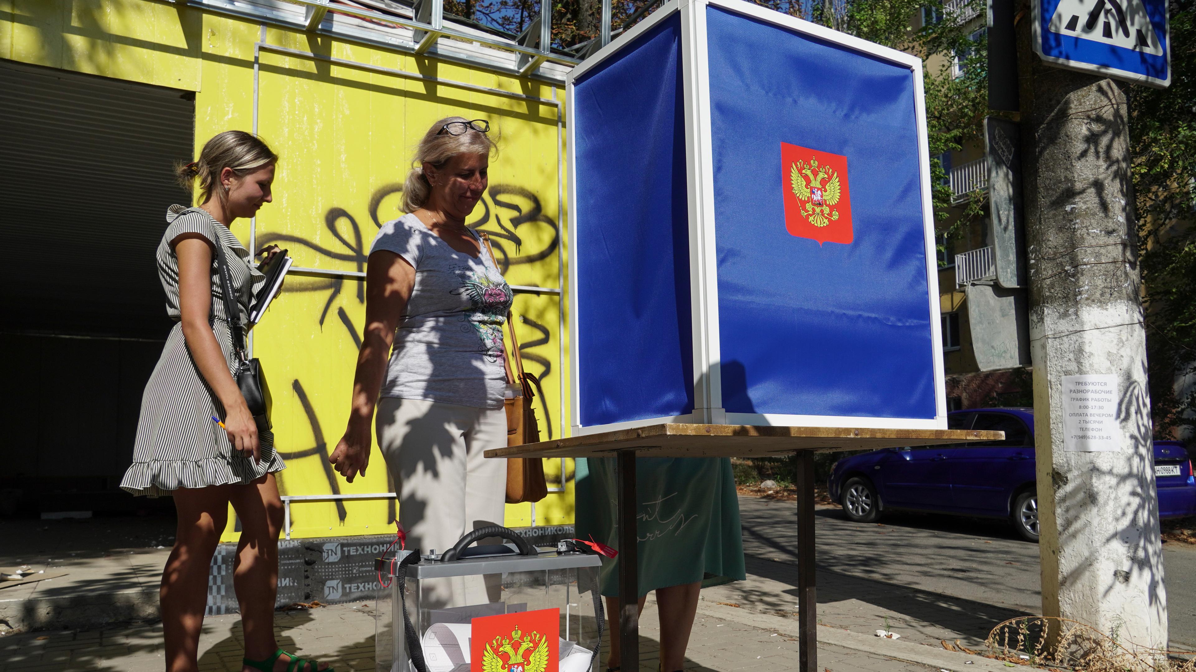 Frauen geben ihre Stimmen in einem mobilen Wahllokal mit dem Wappen Russlands während der vorgezogenen Stimmabgabe für die Kommunalwahlen in Mariupol, aufgenommen am 31.08.2023 