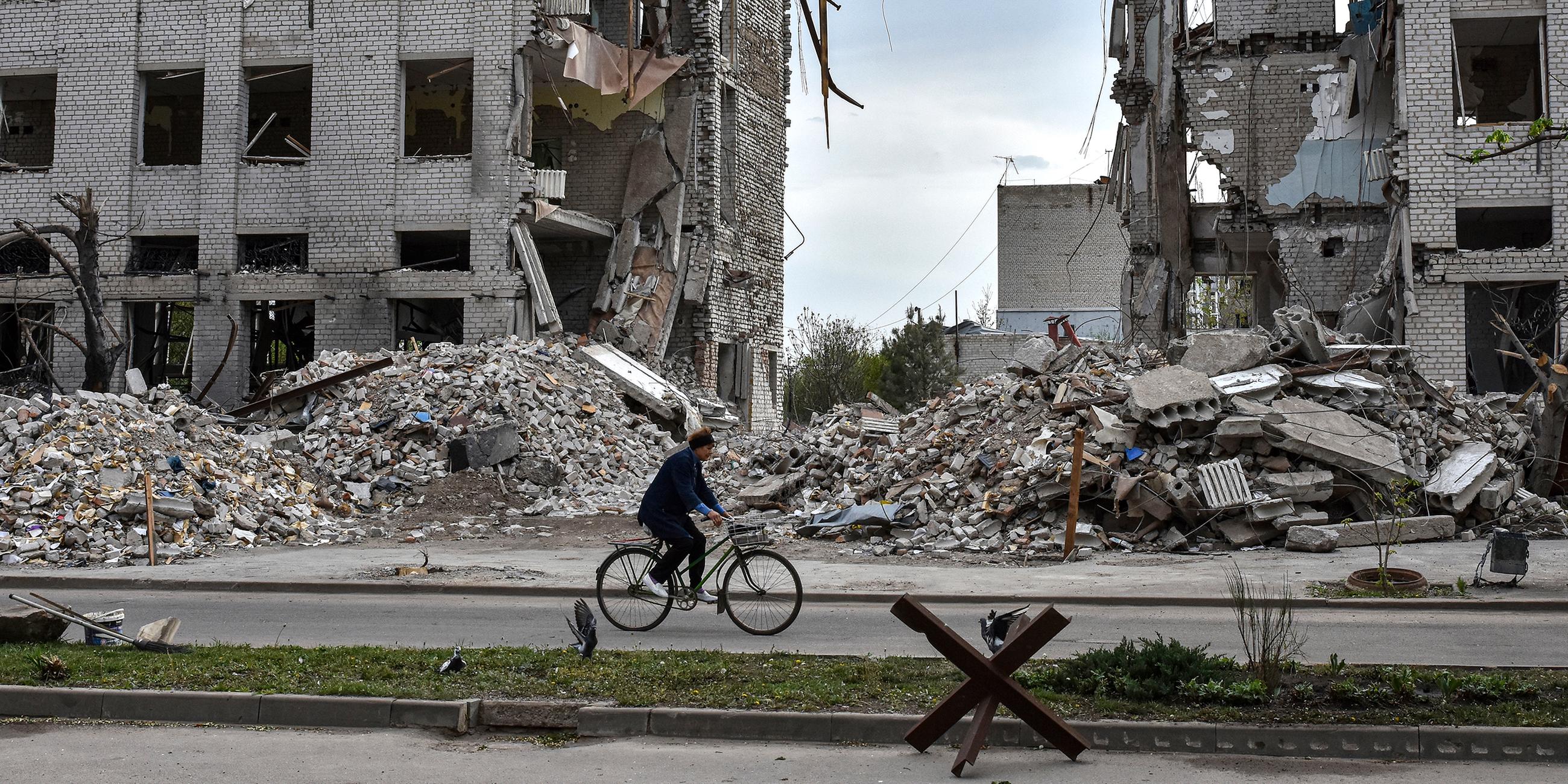 Ukrainerin fährt mit dem Fahrrad vor einem Gebäude, das durch einen russischen Luftangriff zerstört wurde