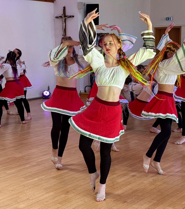 Jugendliche in roten Röcken und kurzen weißen Blusen tanzen in einem Raum.