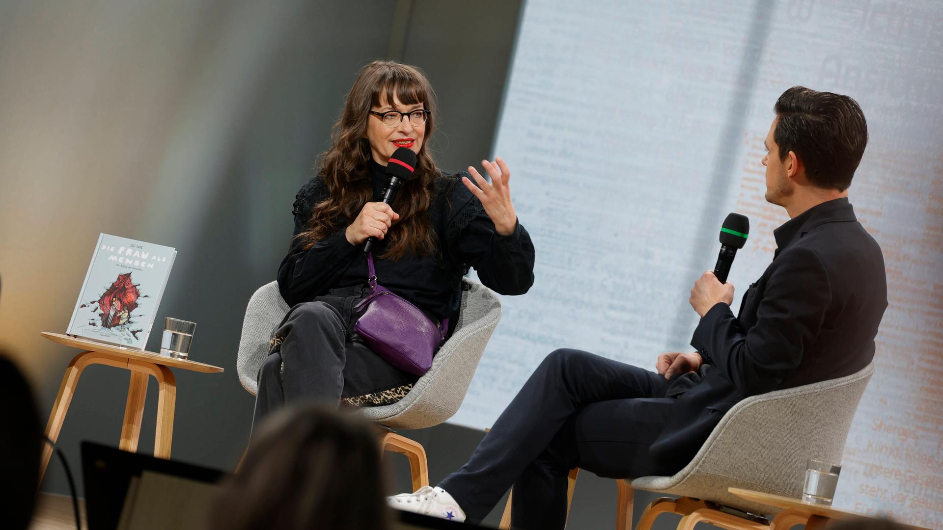 Eine Frau und ein Mann sitzen auf einer Bühne und diskutieren.