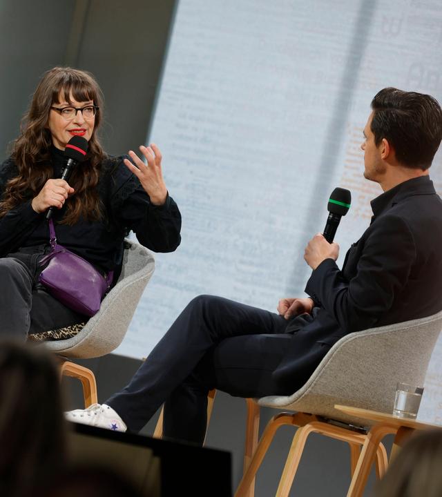 Eine Frau und ein Mann sitzen auf einer Bühne und diskutieren.