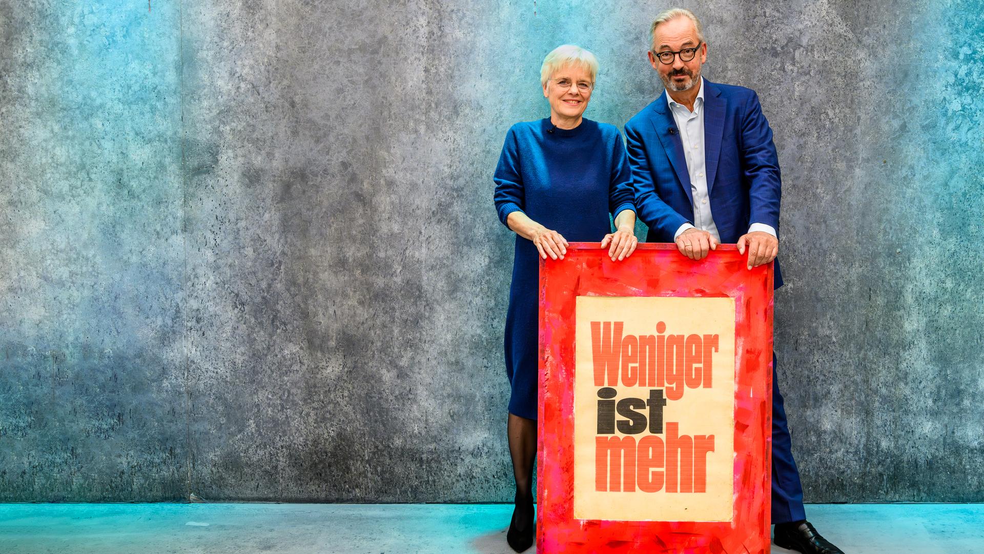 Jan Fleischhauer und Ulrike Herrmann stehen hinter einem Schild auf dem steht: Weniger ist mehr.