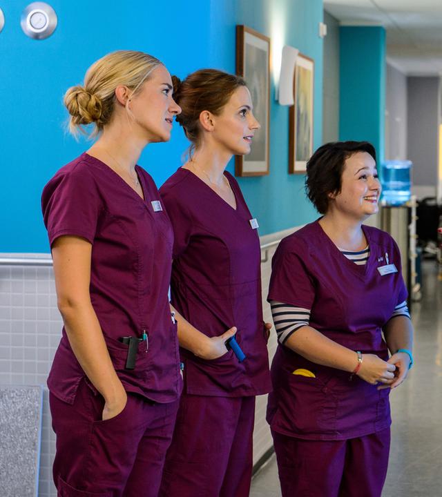 "Bettys Diagnose - Um Haaresbreite": Betty Weiss (Annina Hellenthal), Hanna Winter (Marie Zielcke) und Talula Pfeifer (Carolin Walter) nehmen auf dem Krankenhausflur freudig eine Neuigkeit von Mechthild Puhl (Sybille J. Schedwill) entgegen.