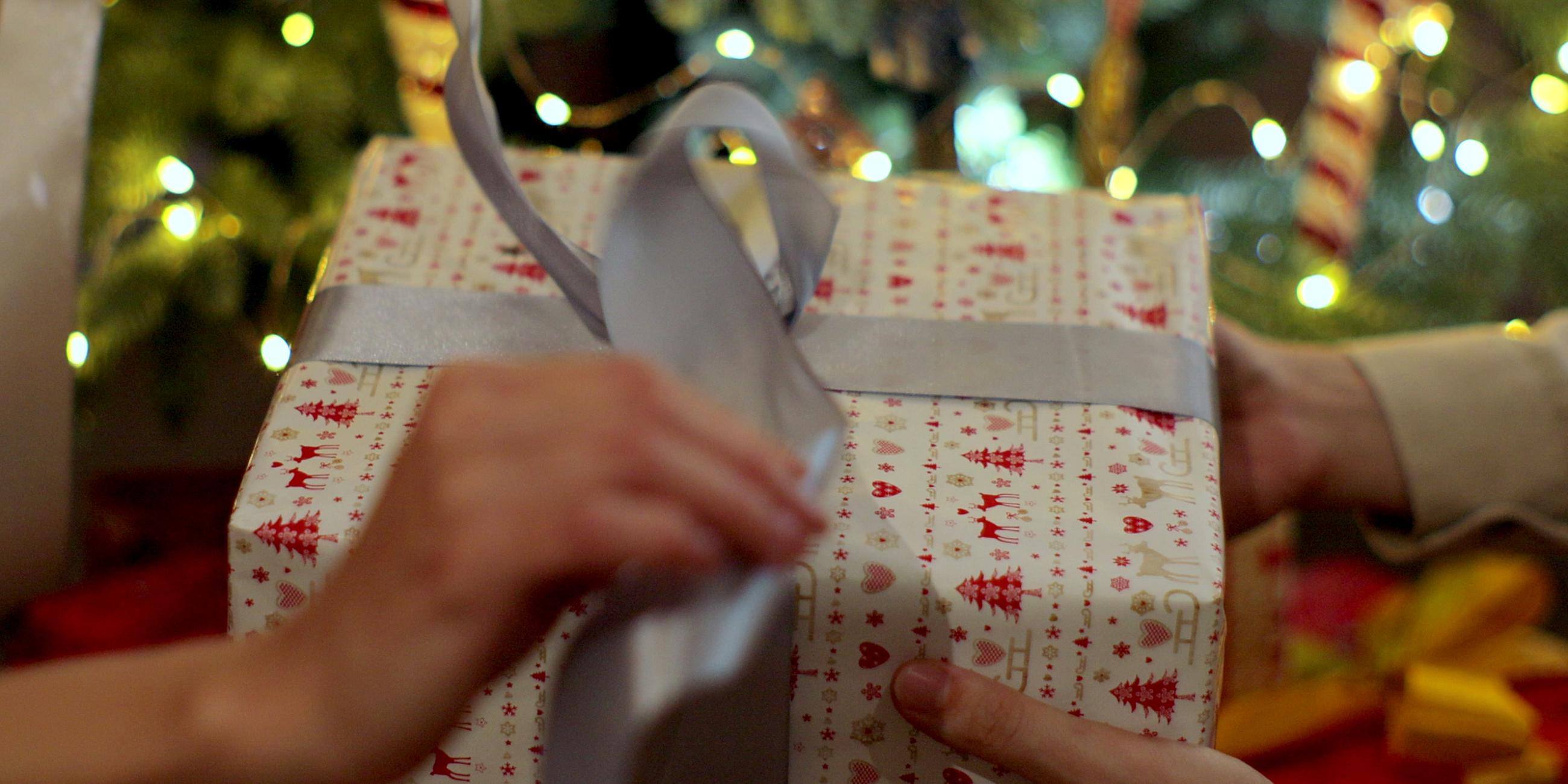 Nahaufnahme der Hände eines Mannes, der einer Frau während der Familienfeier ein Weihnachtsgeschenk überreicht. 