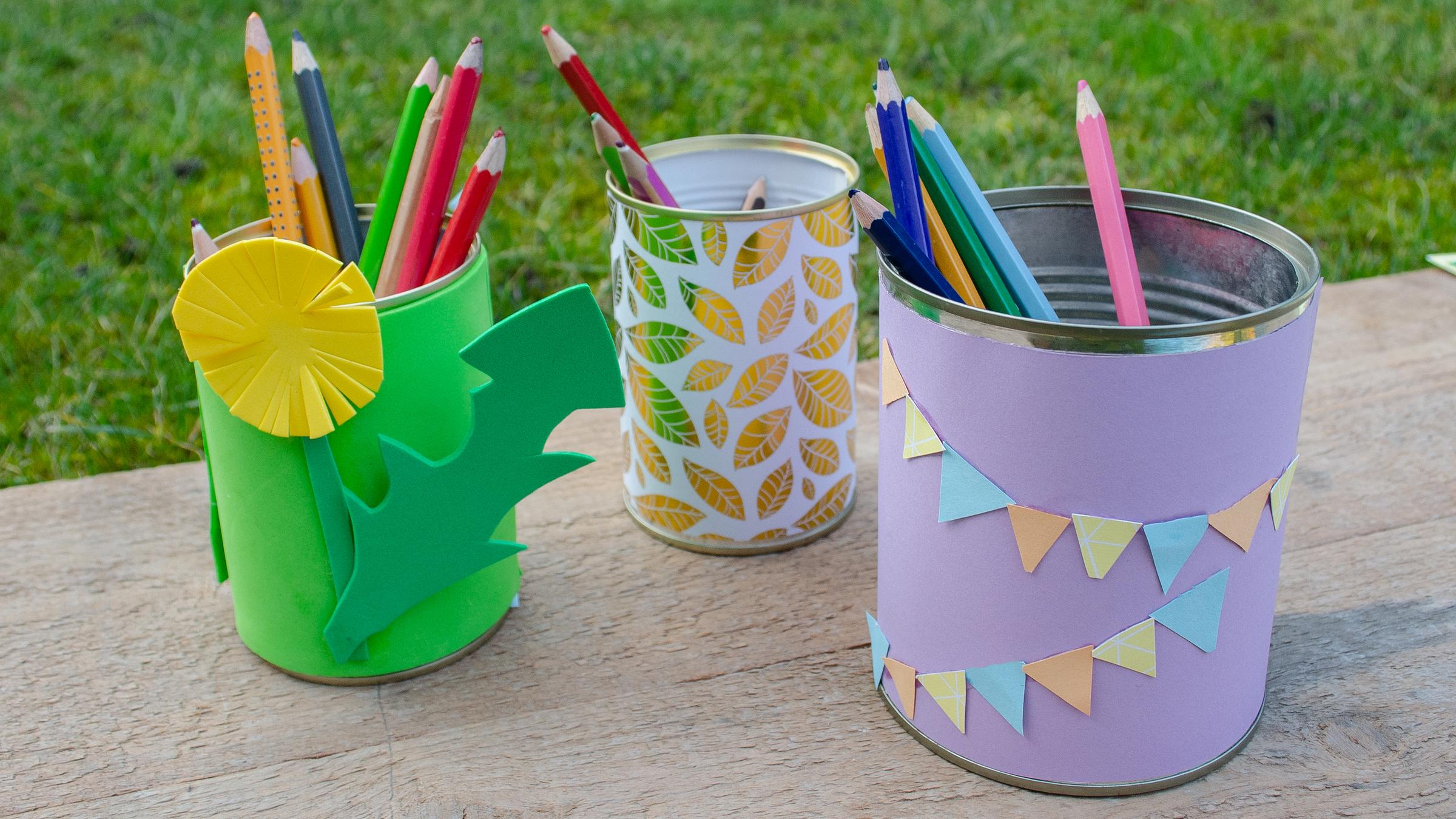 Drei Konservedosen mit buntem Papier umwickelt und Stiften darin.