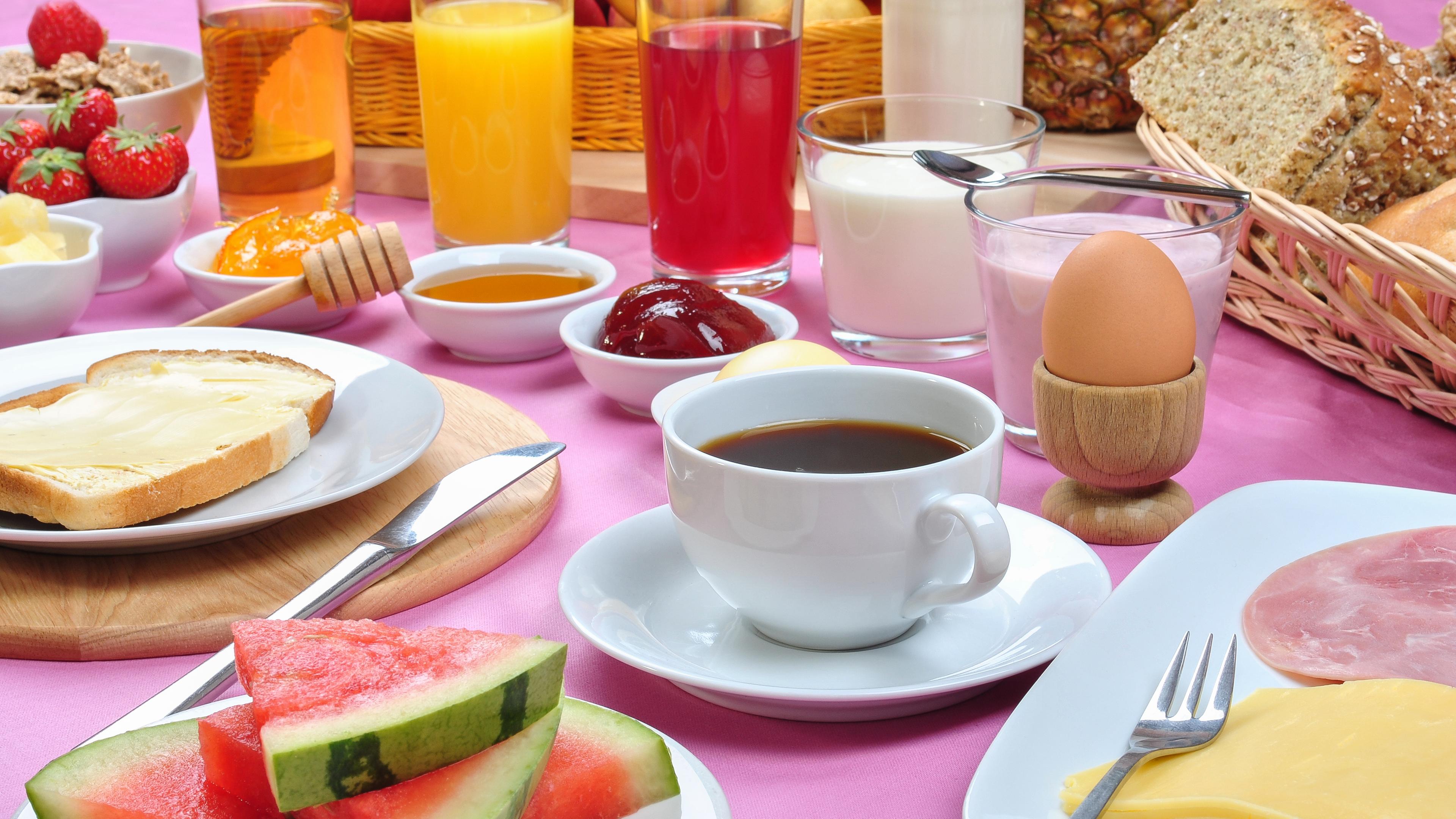 Ein reichlich gedeckter Tisch zum Frühstück: mit Kaffee, aufgeschnittener Wassermelone, Toastbrot, Wurst- und Käsesufschnitt, einem Ei und Saft.