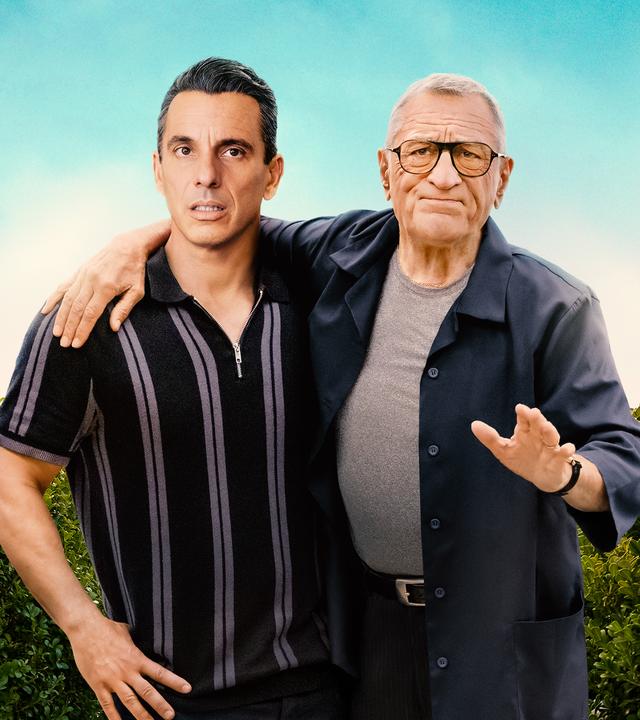 "Und dann kam Dad": Sebastian (Sebastian Maniscalco) und sein Vater Salvo (Robert De Niro) stehen nebeneinander vor einer Hecke und blicken skeptisch nach vorne. Salvo hat einen Arm um seinen Sohn gelegt und macht eine abweisende Geste.
