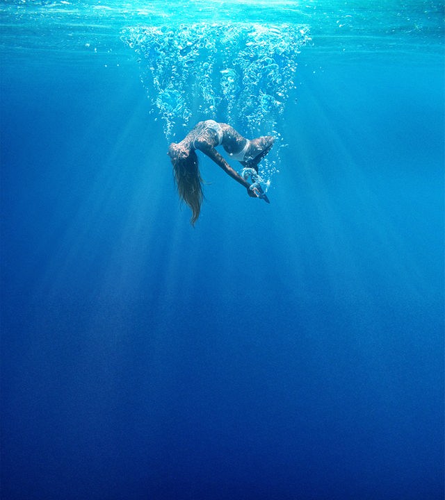 "Under the Silver Lake": Plakatmotiv, Totale, Unterwasseraufnahme: Eine junge Frau (Karen Nitsche) sinkt in gebogener Rückenhaltung in blauem Gewässer in Richtung Grund. An der Wasseroberfläche schimmert Sonnenlicht.