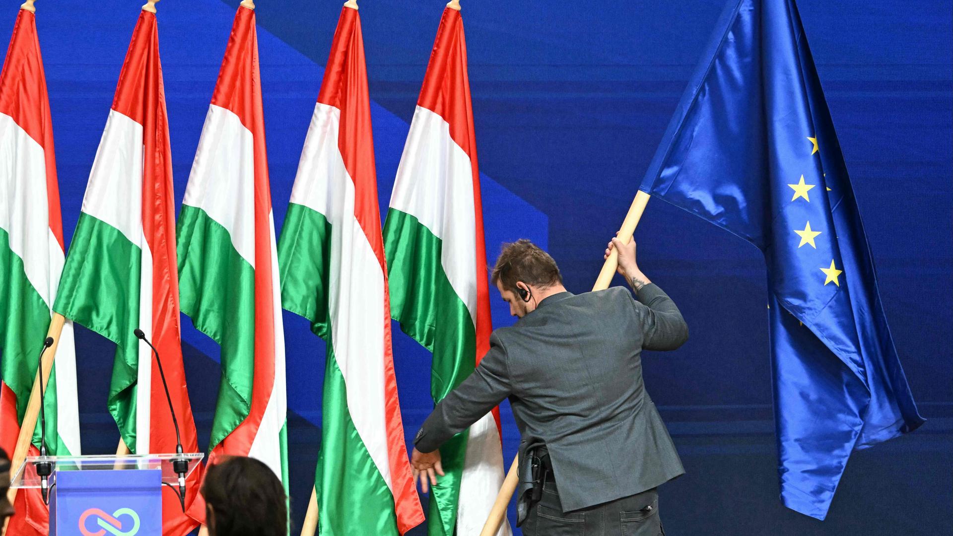 Mann stellt Europa-Flagge zu einer Reihe von ungarische Flaggen hinter einem Redner-Pult.