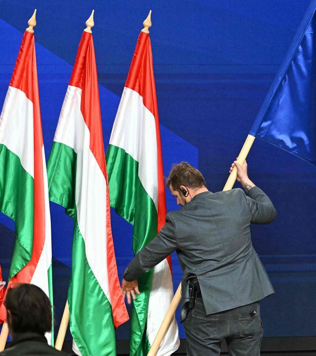 Mann stellt Europa-Flagge zu einer Reihe von ungarische Flaggen hinter einem Redner-Pult.