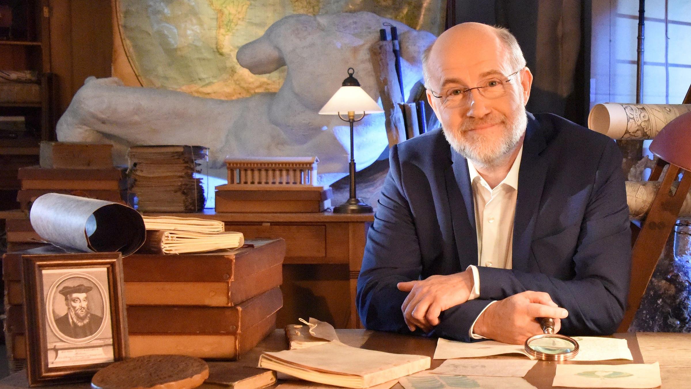 Prof. Lesch sitzt an einem Schreibtisch und schaut in die Kamera.