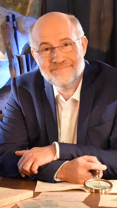 Prof. Lesch sitzt an einem Schreibtisch und schaut in die Kamera.