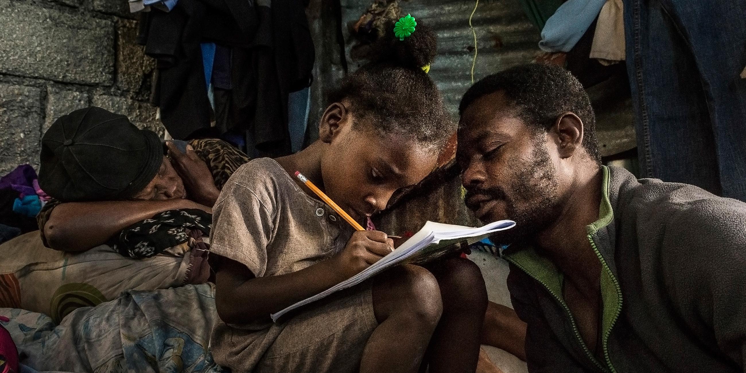 Vater auf Haiti hilft seiner 7-jährigen Tochter bei den Hausaufgaben 