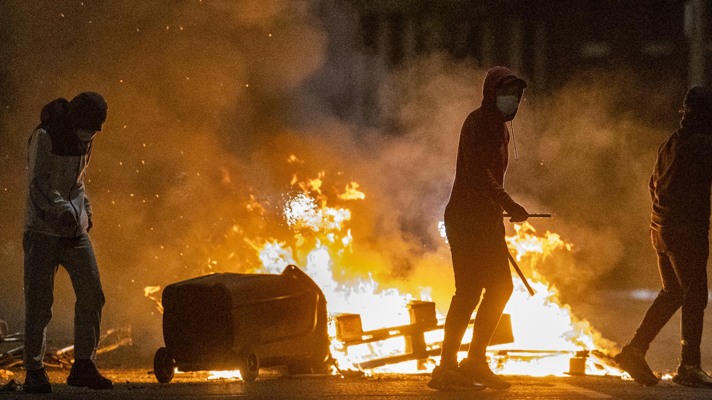  Menschen stehen während weiterer Unruhen neben einem Feuer in einer Straße in Belfast. In der britischen Provinz Nordirland kommt es seit Tagen zu nächtlichen Krawallen, bei denen inzwischen mehr als 40 Polizisten verletzt wurden.